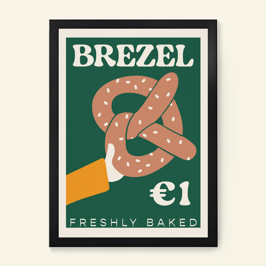 A framed art print featuring a retro-style advertisement for a freshly baked pretzel. The design has a dark green background with the word 'BREZEL' in bold white letters at the top, a large illustrated pretzel in the centre. 