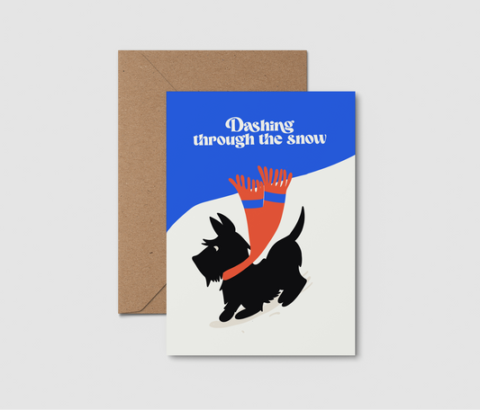 A6 holiday greeting card with a brown kraft envelope, featuring a black Scottie dog wearing a red scarf against a blue and white background with the text 'Dashing through the snow'.