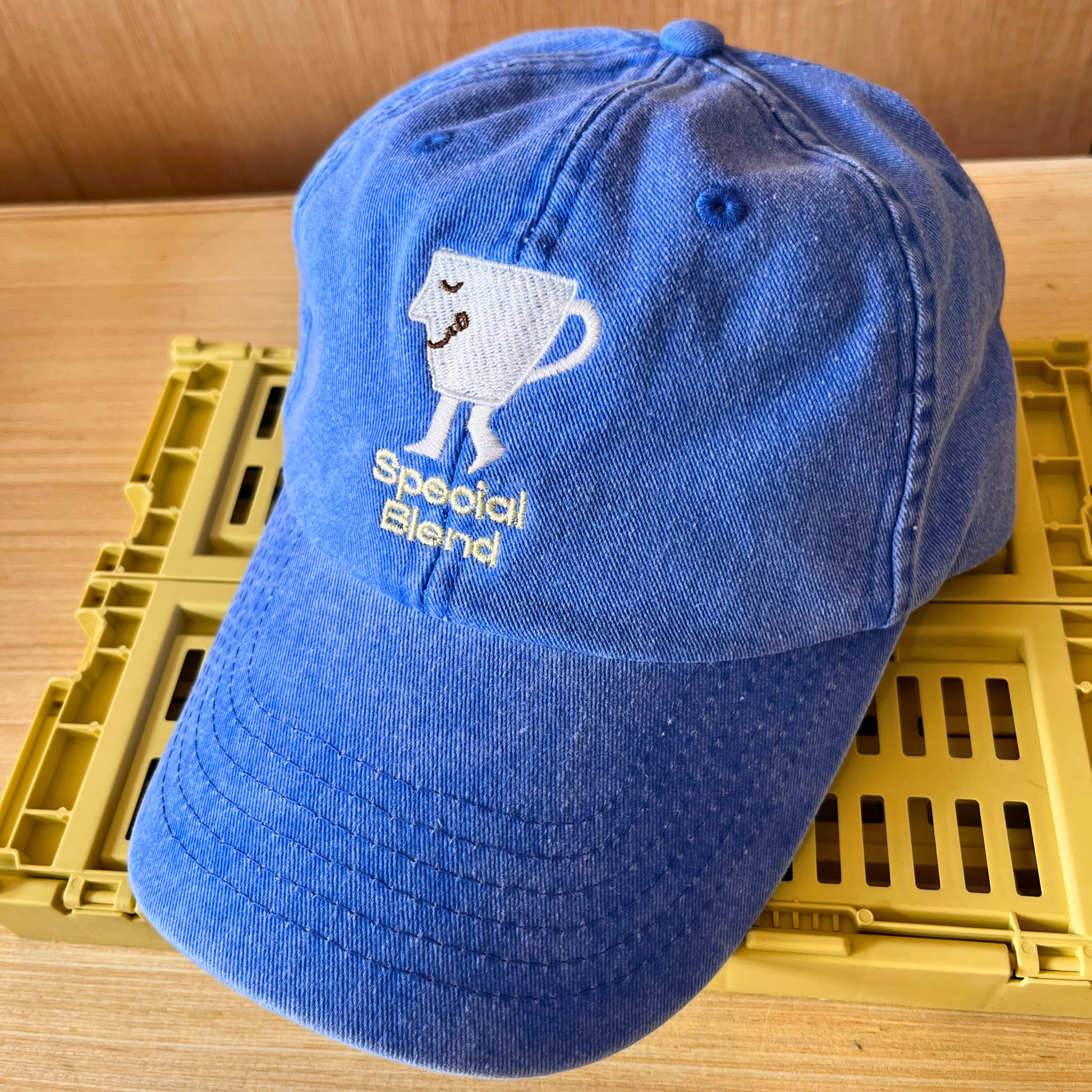 A blue cotton baseball cap with an embroidered white coffee cup character and the words 'Special Blend' on the front. Men's fashion cap. 