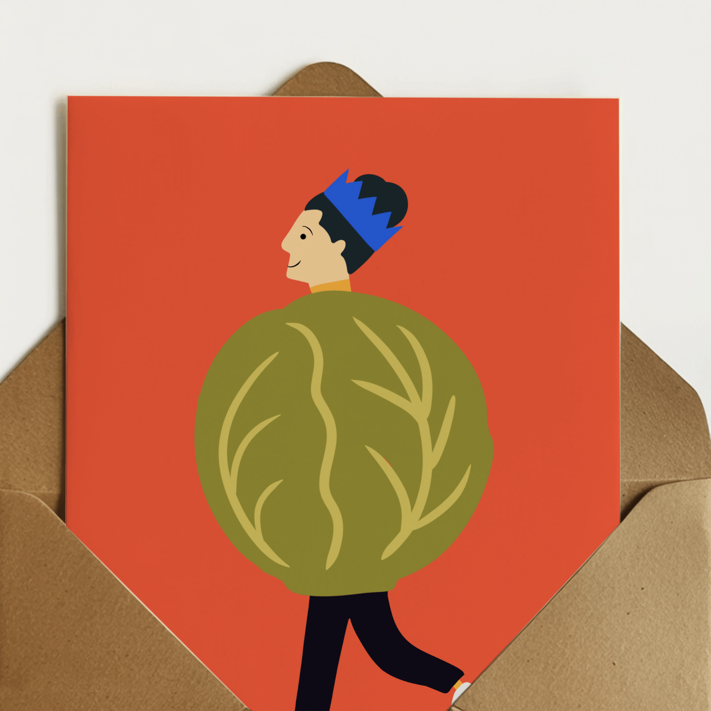 A6 greeting card with a bold orange-red background and an illustration of a person wearing a brussel sprout, shown standing in front of a brown kraft envelope.